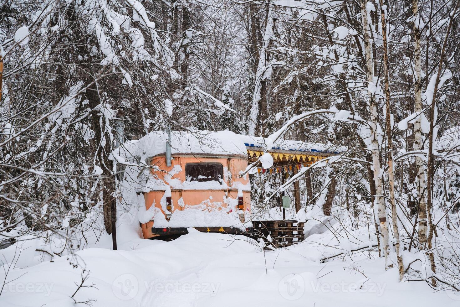 An orange trailer, which stands out vividly, is completely covered in a thick layer of snow in the middle of a beautiful, snowy forest that is enveloped in winters chill photo