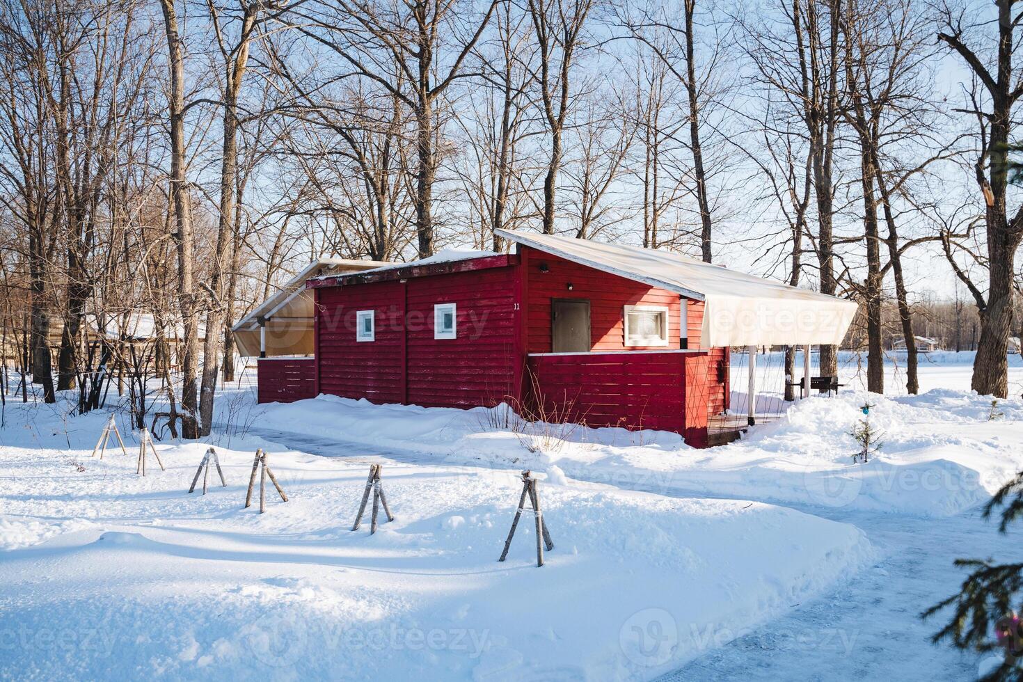 In a stunningly beautiful snowy forest, a charming and vibrant red house stands proudly, surrounded by tall, majestic trees, their branches gracefully adorned with fluffy white snowflakes photo