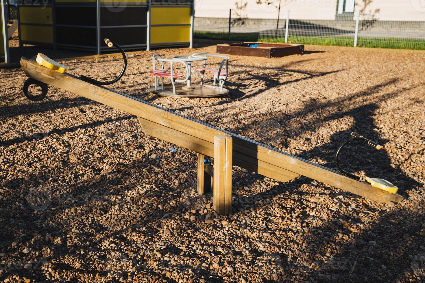 A wooden seesaw is resting on the dirt ground in a childrens playground, surrounded by a vibrant landscape with various textures, inviting kids to play and enjoy their time outdoors photo