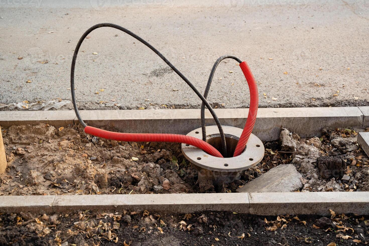 An exposed electrical junction box displaying red and black wires located on an urban sidewalk, posing a hazard photo