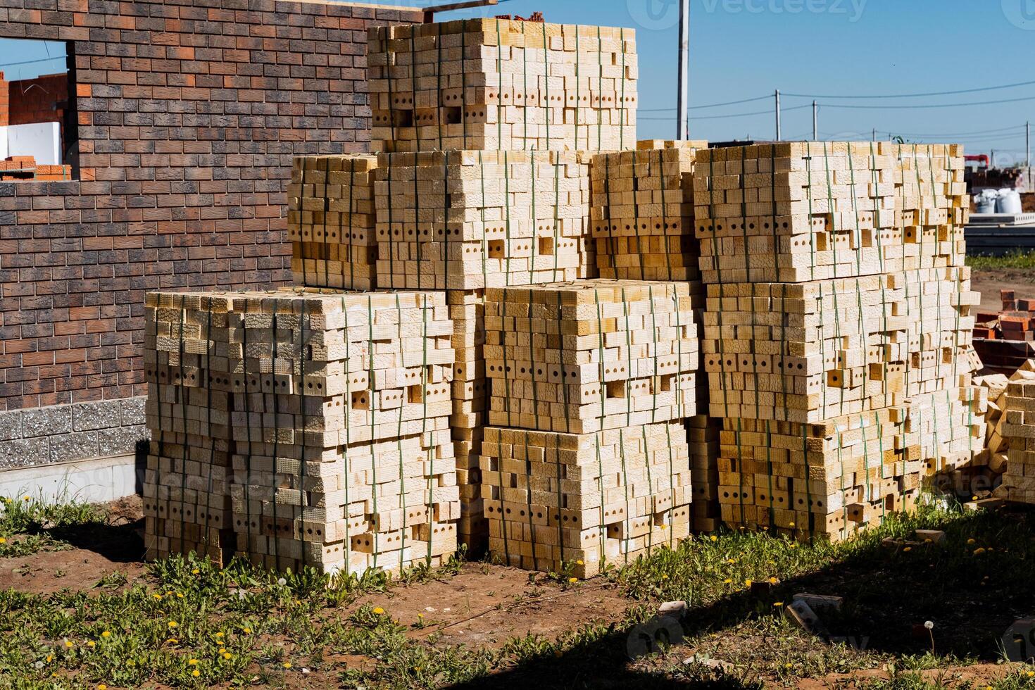 The neatly stacked wooden pallets at a construction site by a brick building under a clear sky symbolize progress in the infrastructure sector and efficient materials management photo