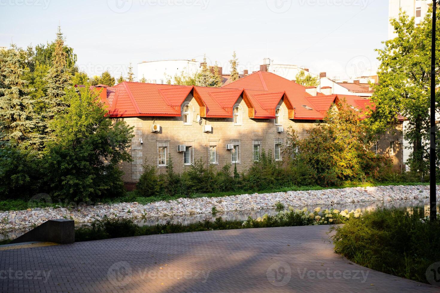 The charming house features a vibrant red roof and is surrounded by lush trees and colorful bushes that enhance its beauty and blend it harmoniously into the natural landscape around it photo