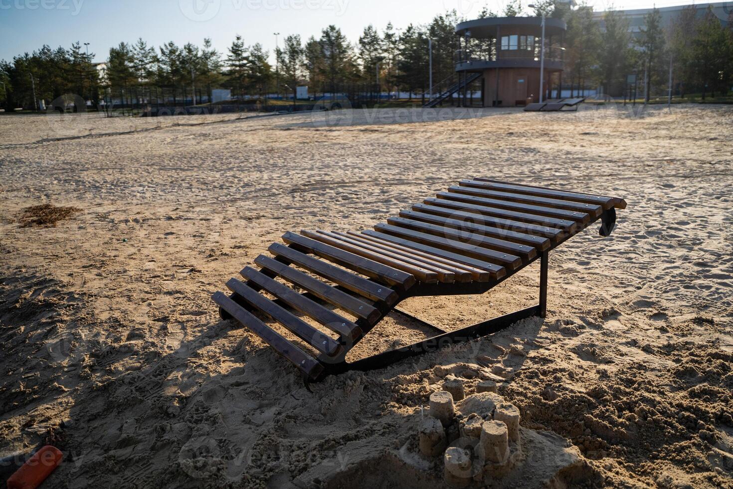 A beautifully crafted wooden lounge chair is positioned on the sandy beach, right next to an intricately built sand castle, both capturing the wonderful essence of summer fun and relaxation photo