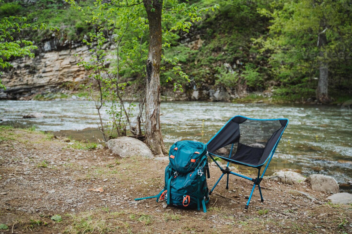 Backpack and chair resting by river in natural landscape photo