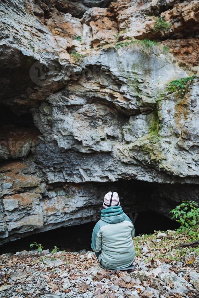 A person is sitting comfortably on the ground directly in front of a cave, taking in the beautiful scenery and completely enjoying the breathtaking natural beauty that surrounds them photo