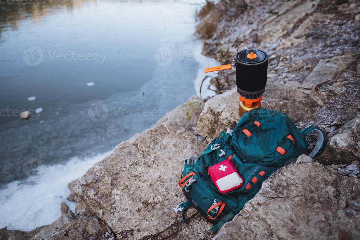 Camping equipment lies on a rock near the water, a camping burner, a cooking system. First aid kit, camping in nature. photo