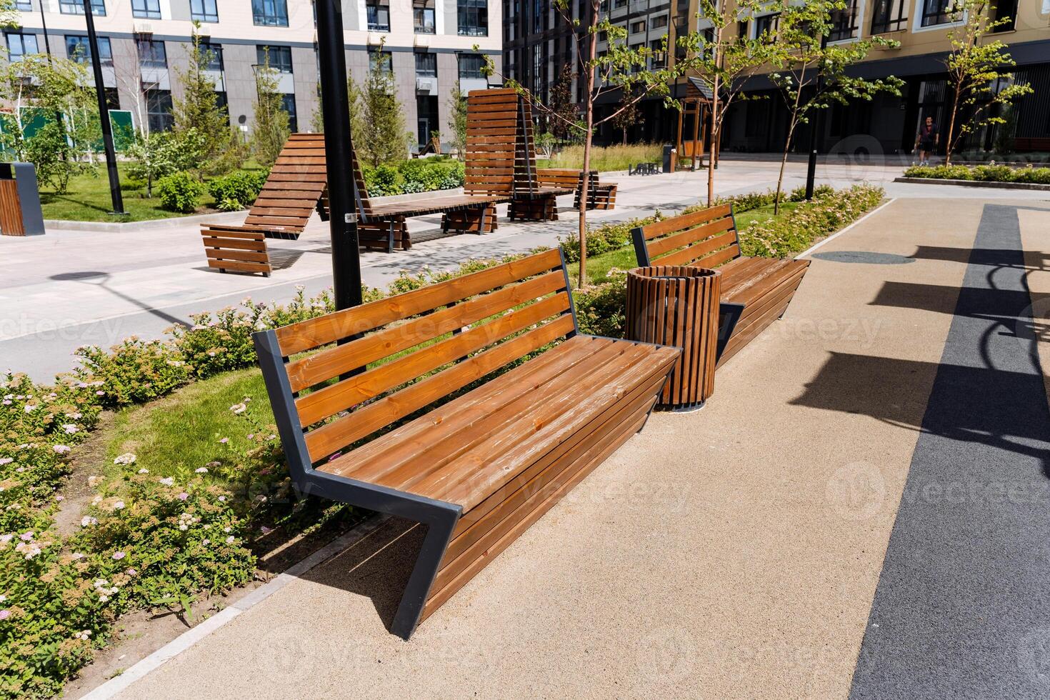 A scene of a modern urban park with benches and walkways in bright summer daytime, surrounded by buildings, greenery, and nature, ideal for relaxation and recreation photo