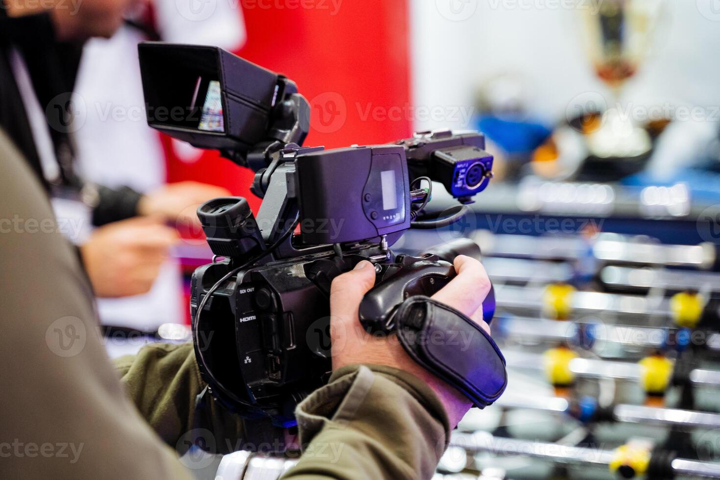 A man is currently holding a camera securely in his hands right in front of a foosball table, ready to capture the exciting action or fun moments taking place there photo