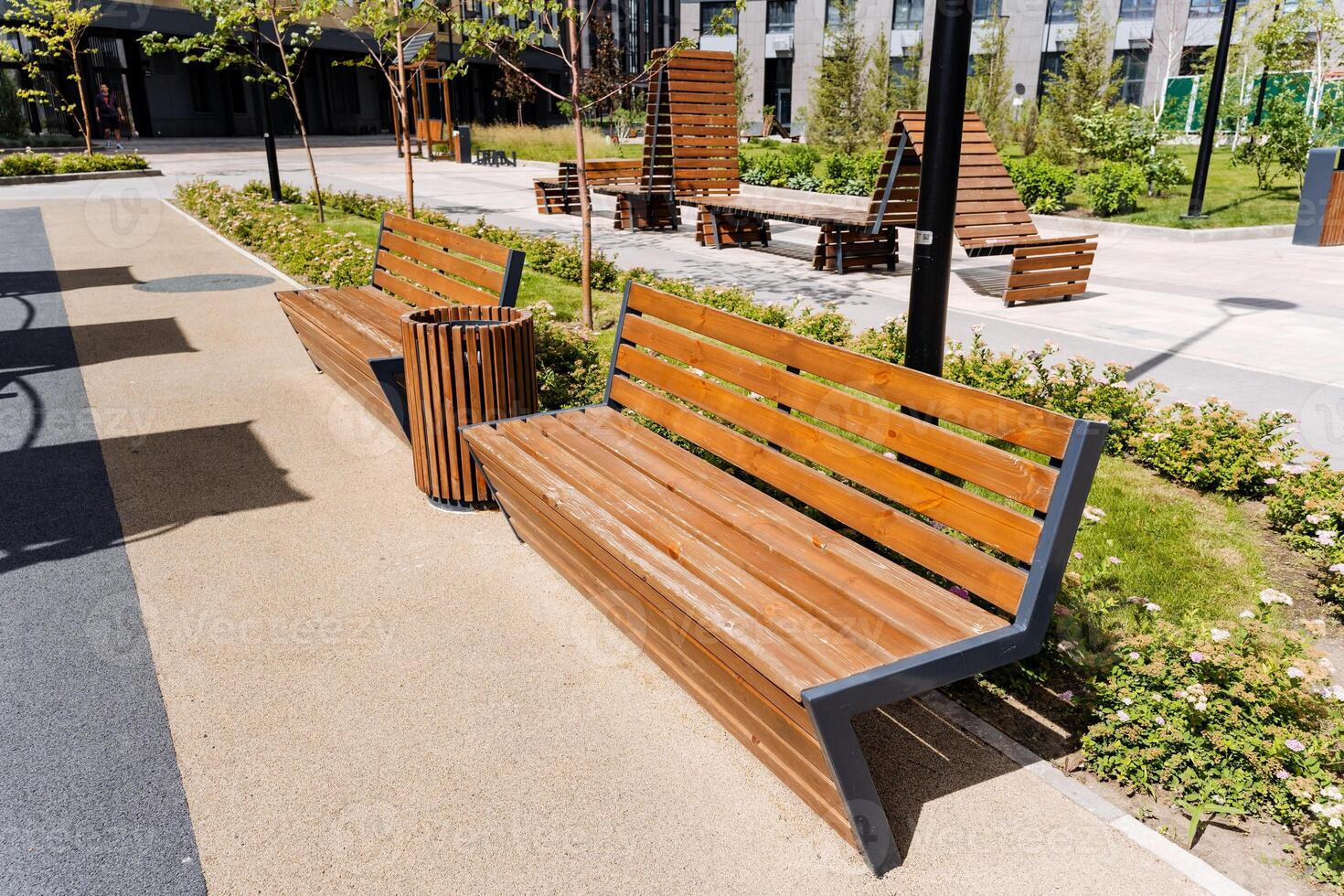 In the park, there is a row of wooden benches and a trash can placed amidst lush green grass. This outdoor space harmoniously combines natural elements with urban design photo