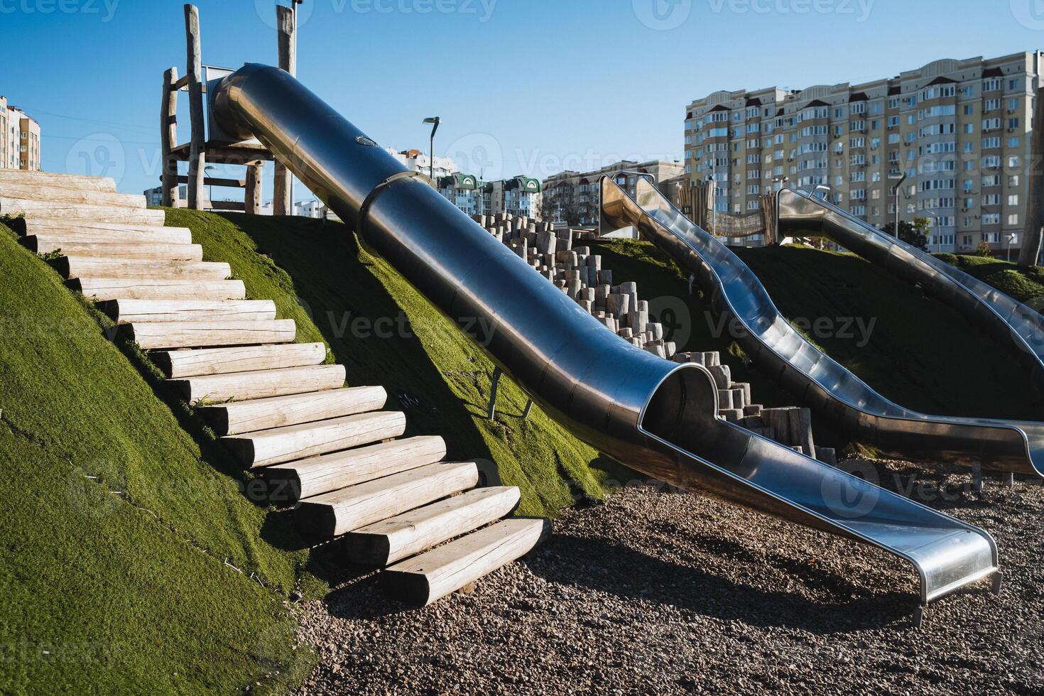 A playground features a shiny stainless steel slide, complemented by a sturdy set of stairs that lead up to the top, making it an exciting attraction for children to enjoy their playtime photo