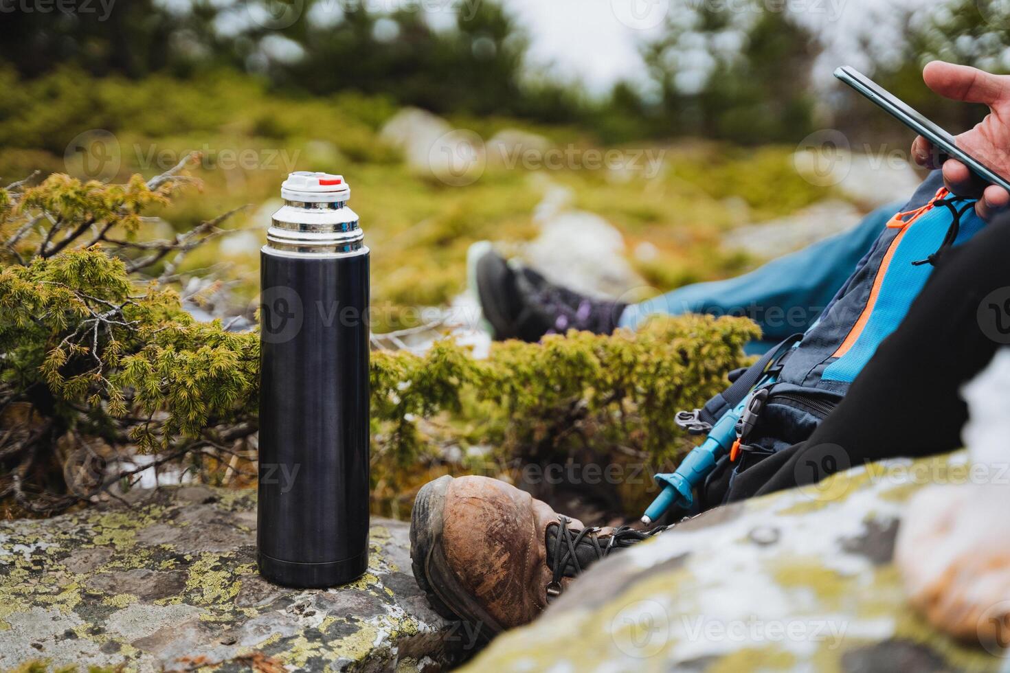 a person is sitting on a rock with a thermos and a cell phone photo