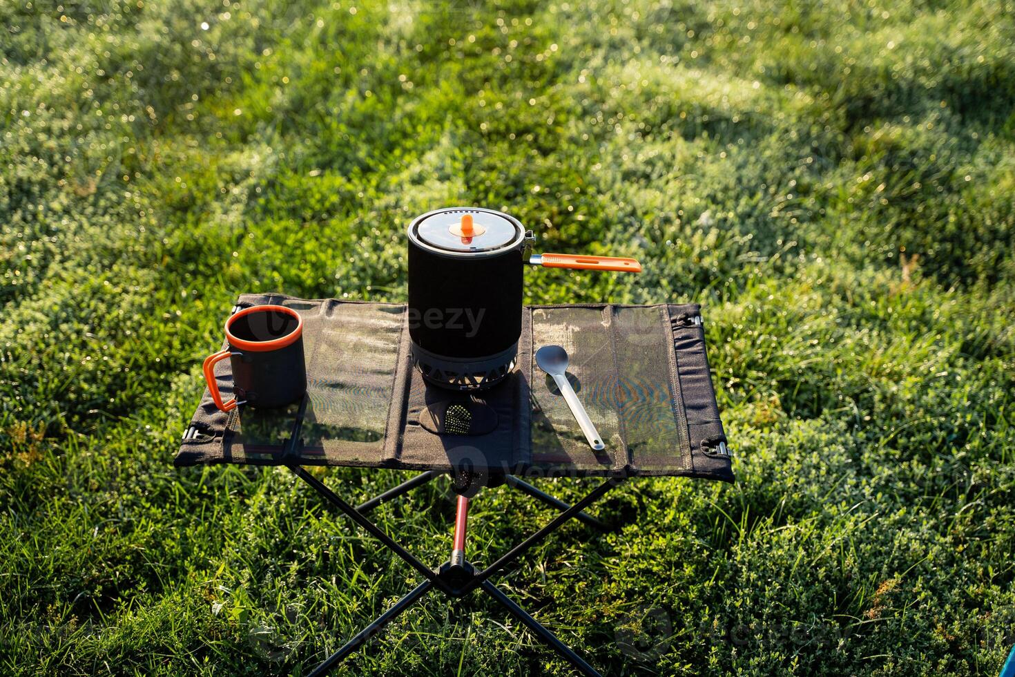 A table with a pot , cup and spoon on it in the grass photo