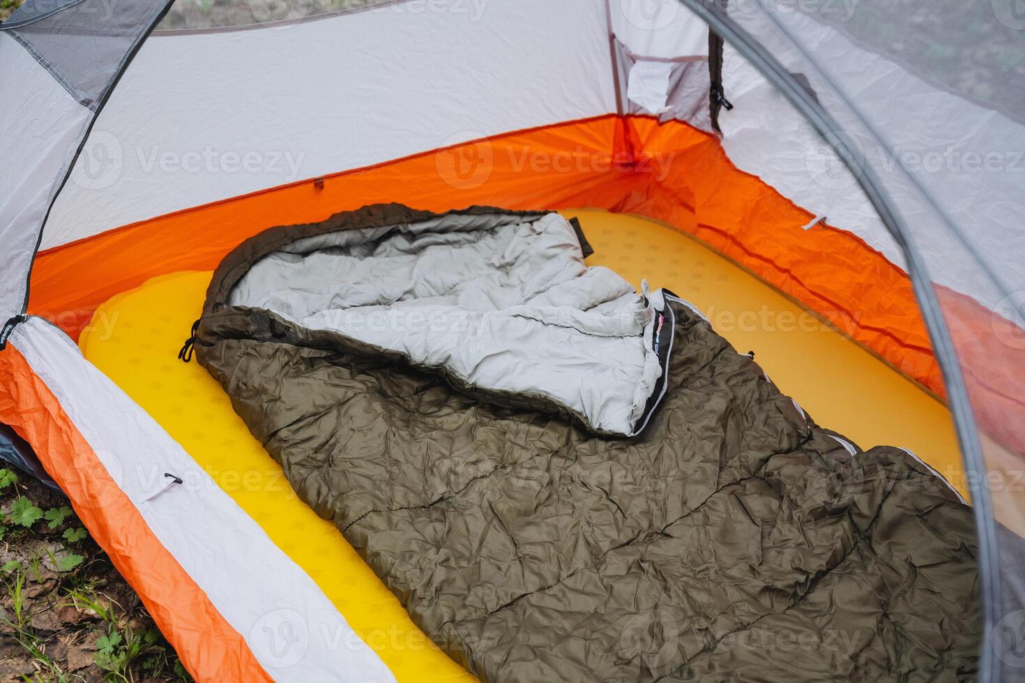 A sleeping bag rests inside a tent on the grassy slope under the shade of a roof photo