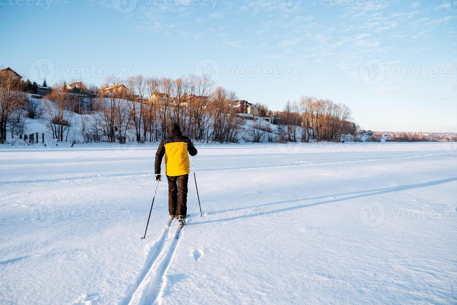 Rear view of skier walking on field in winter, man laying trail on deep snow. A lonely traveler in the snowy desert. photo