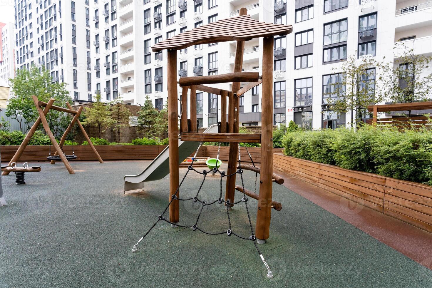 There is a wooden playground featuring a slide and swings situated right in front of a building, providing a fun recreational space for children and families to enjoy together photo