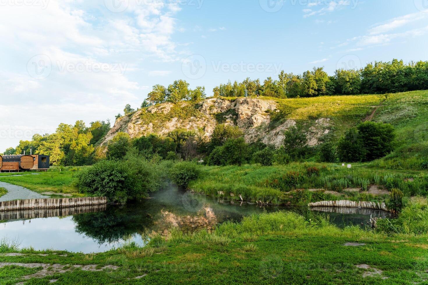 A mesmerizing view is presented as a beautiful train passes peacefully by a tranquil lake surrounded by lush greenery under a captivating sky with fluffy clouds overhead photo