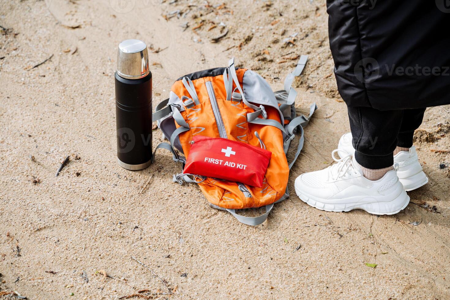 A person next to a first aid kit and backpack on the sandy beach photo