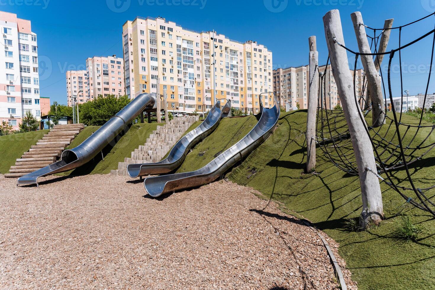 The playground provides a range of slides set against a cityscape backdrop in an urban environment with asphalt and a condominium facade, creating a distinctive leisure experience photo