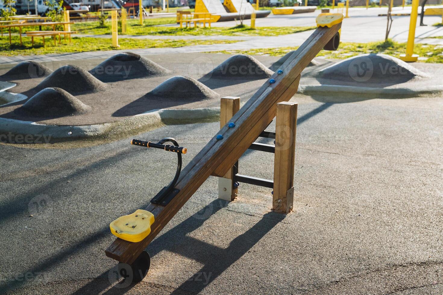 In a vibrant playground, there is a wooden seesaw featuring a bright yellow seat, inviting children to enjoy their time outdoors on this fun piece of recreational equipment photo