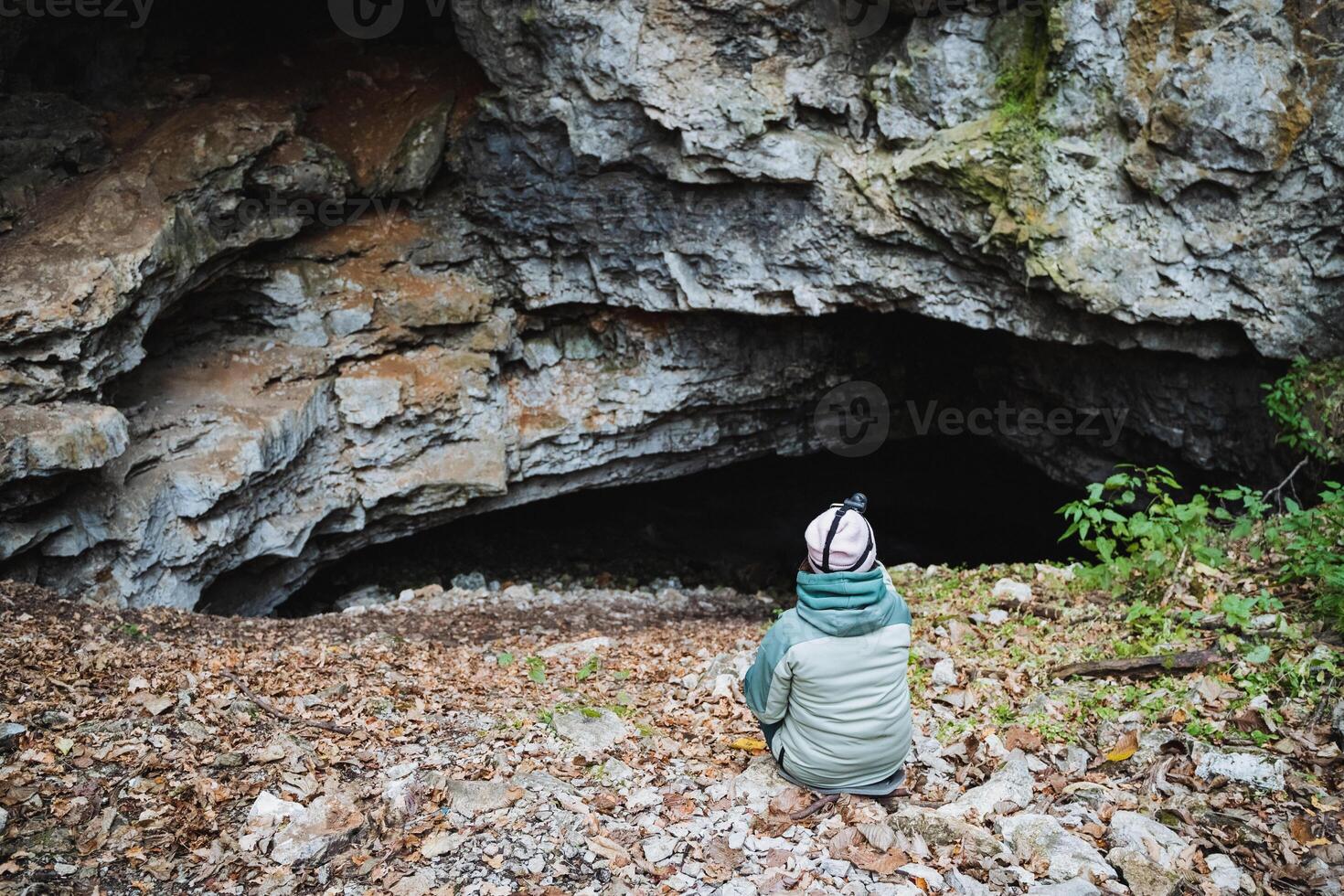 A person is comfortably seated on the ground in front of a large cave entrance, enjoying the natural beauty of the surroundings and the unique geological features nearby photo