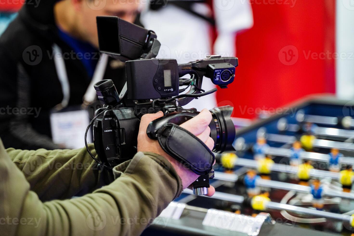 A man is standing and holding a camera in front of a foosball table, which is a popular arcade game that involves players manipulating rods to kick a ball into the opposing goal photo
