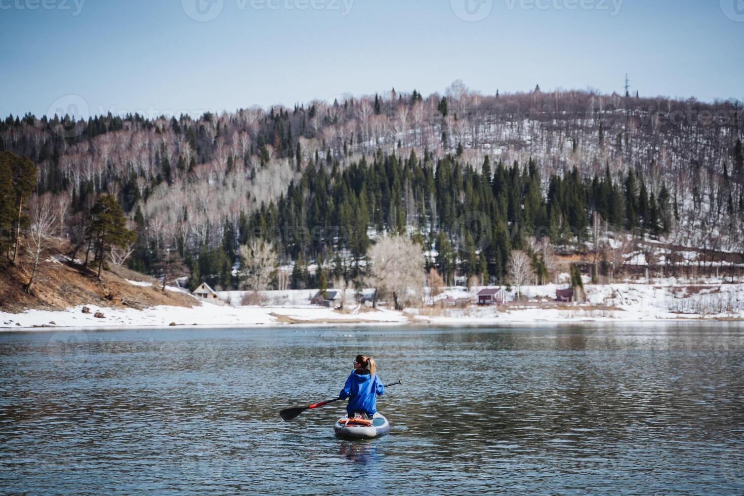 Woman floating on a stand-up paddle board on the river against the background of mountains, beautiful landscape, view from the water, man sitting on a board with a paddle. photo