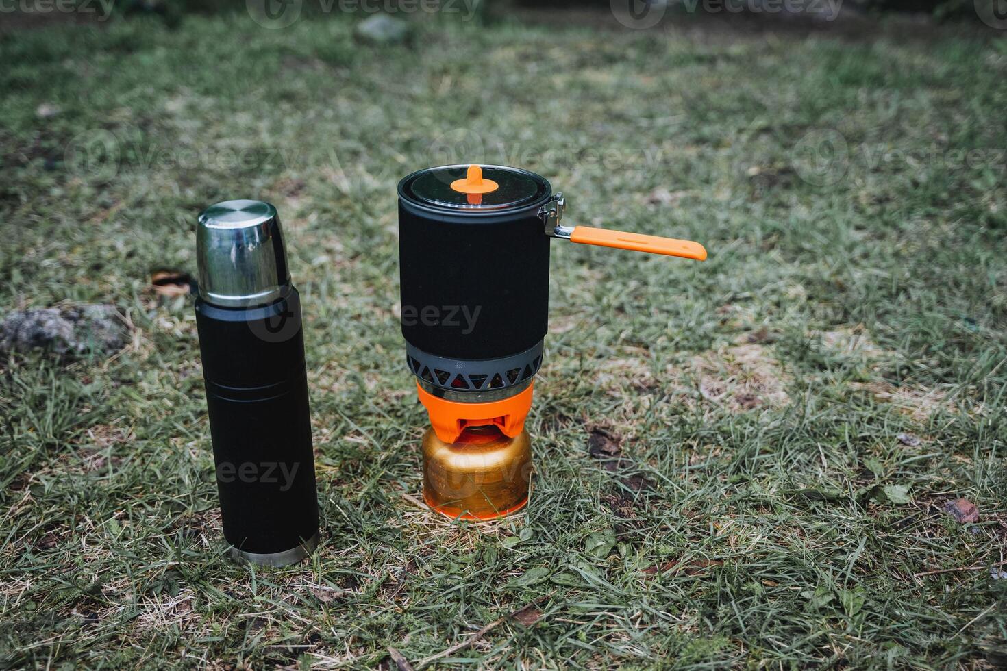 Thermos and pot placed on grass near stove fueled by gas photo