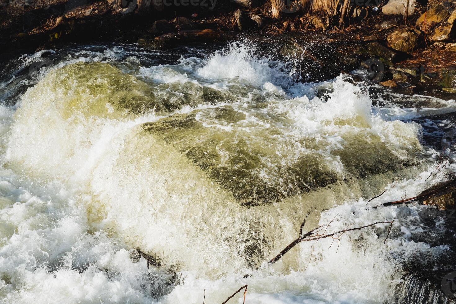 In the center of a flowing river, there is a large rock that stands prominently, creating an interesting feature within the natural landscape surrounding the watercourse photo