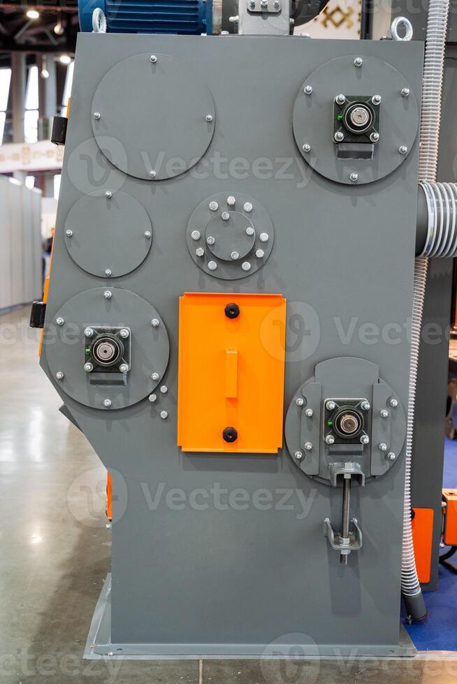 A large, robust industrial machine, which is characterized by its gray and orange coloring, is presently positioned on a smooth, durable concrete floor within a workshop or factory setting photo
