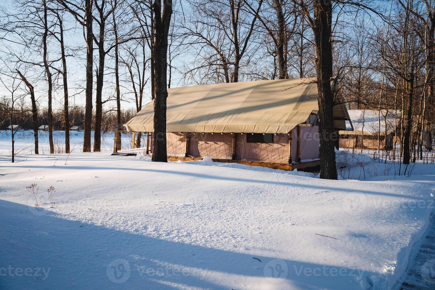 In the heart of a beautiful, snowy forest, there stands a quaint little house surrounded by tall trees, blanketed in white, creating a serene winter wonderland atmosphere photo