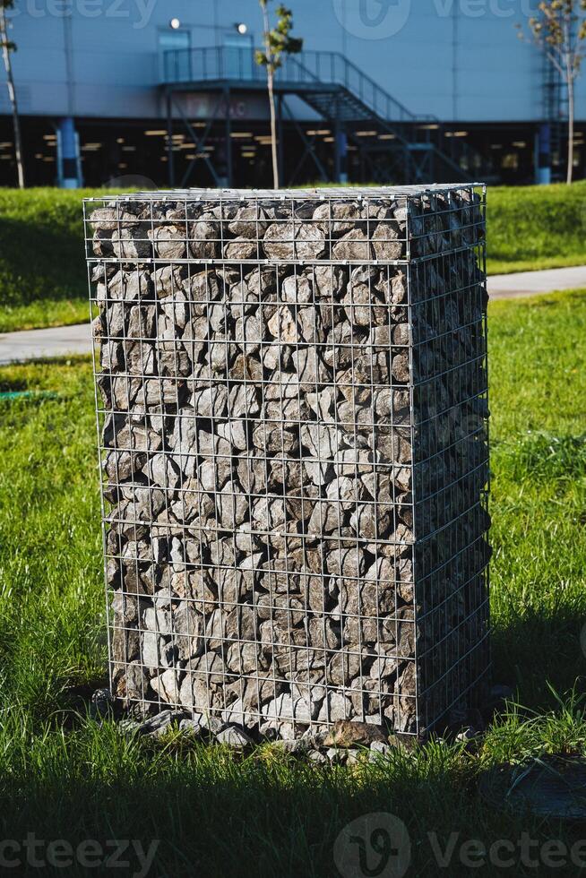 A large and imposing rock wall is positioned prominently in the lush green grass that lies right in front of a building, creating a striking visual contrast in the landscape photo