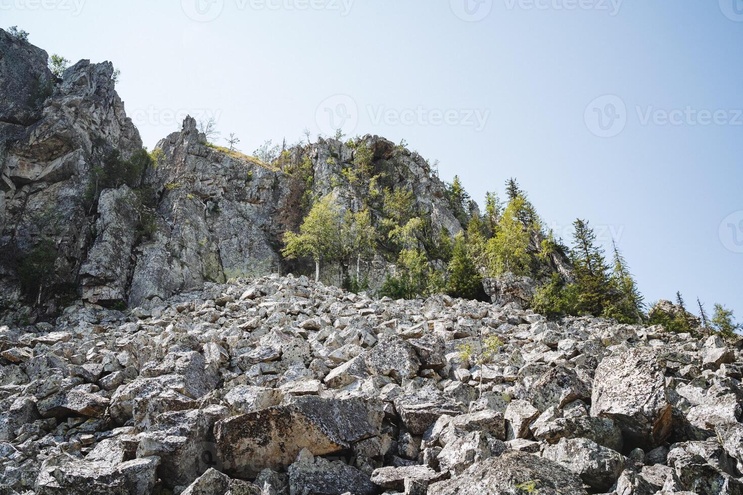A picturesque natural landscape emerges from a rocky hillside adorned with trees, blending the sky, mountain, and terrestrial plants into a harmonious tapestry of elements photo