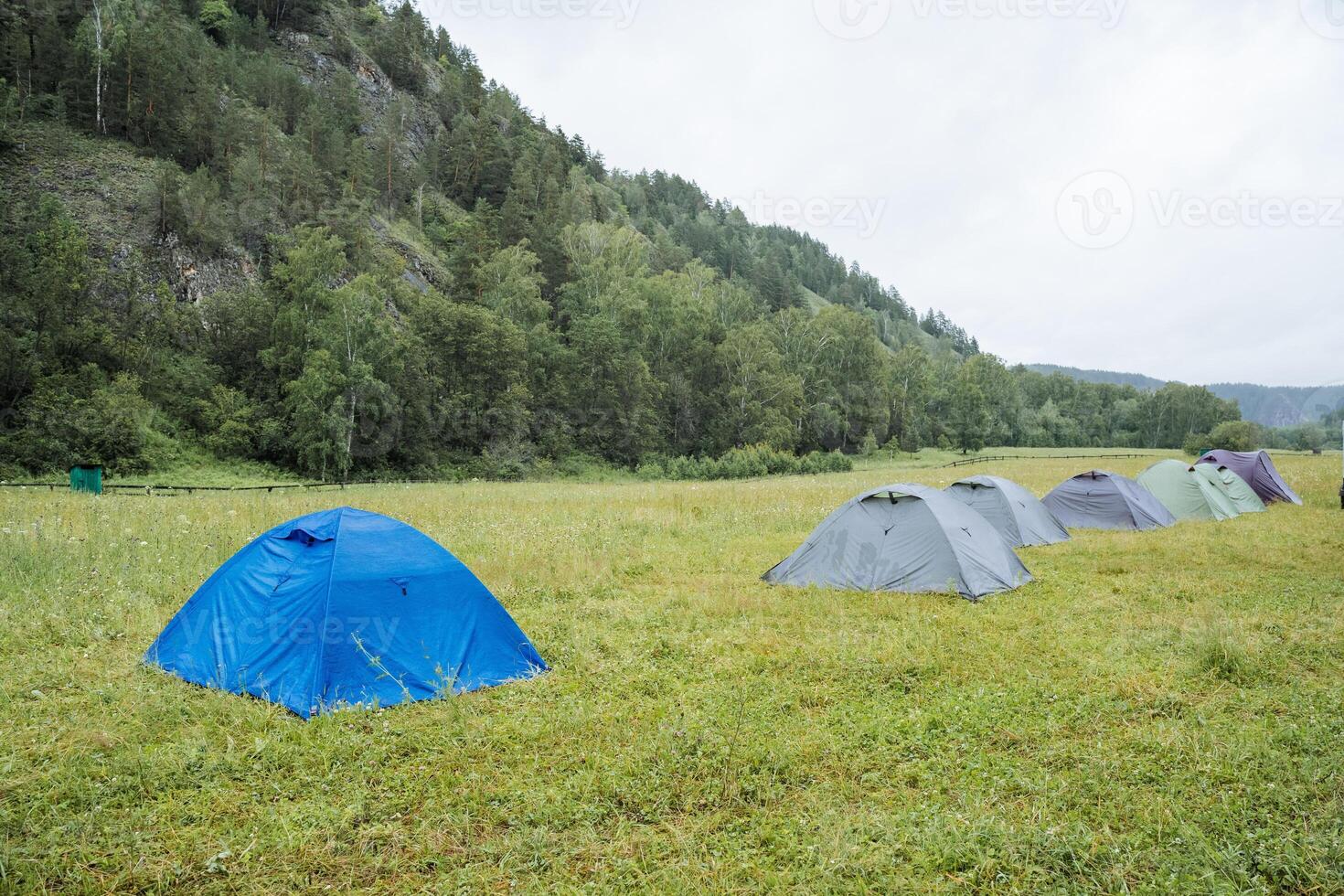 Scenic Outdoor Camping A Line of Tents Set in a Verdant Meadow Near Forested Hills, providing a perfect getaway into nature and wilderness for relaxation and exploration photo