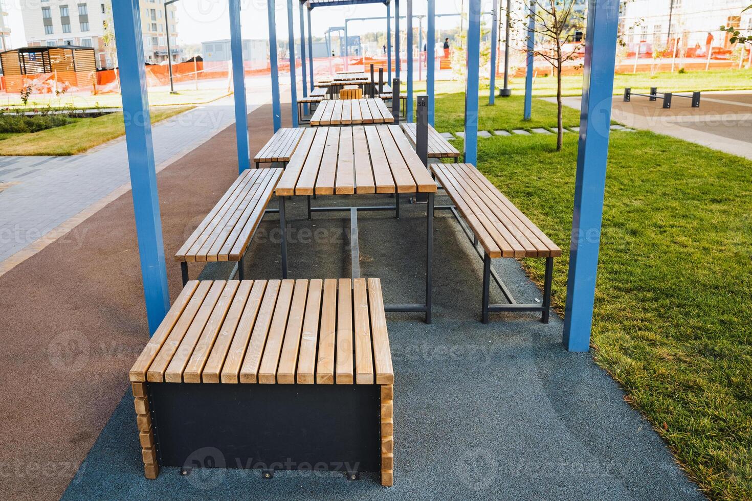 In a scenic park, there is a delightful row of sturdy wooden picnic tables accompanied by benches, providing a perfect spot for leisure activities and relaxation amidst the greenery photo