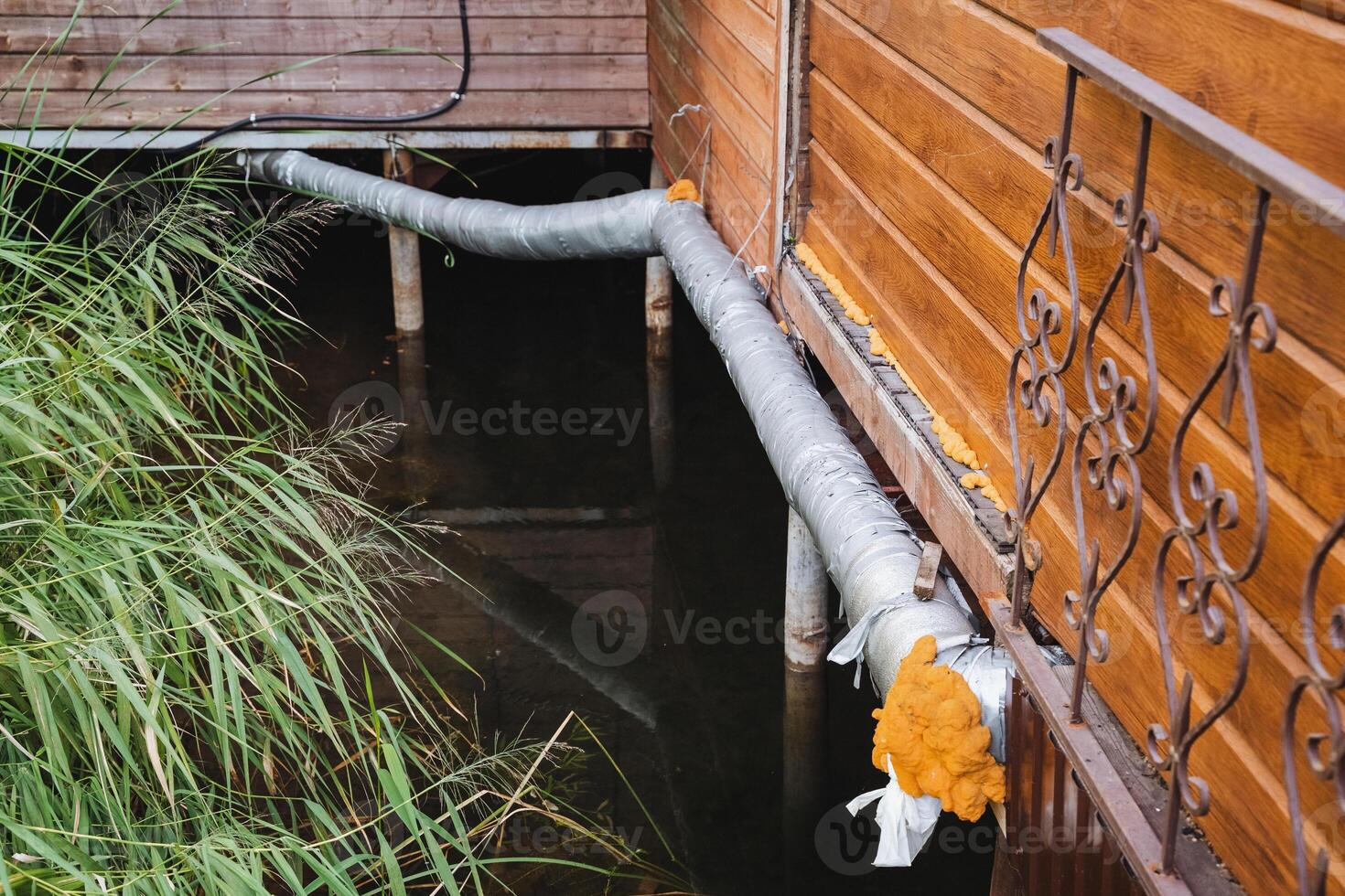 A hose is connected to a wooden building next to a body of water photo