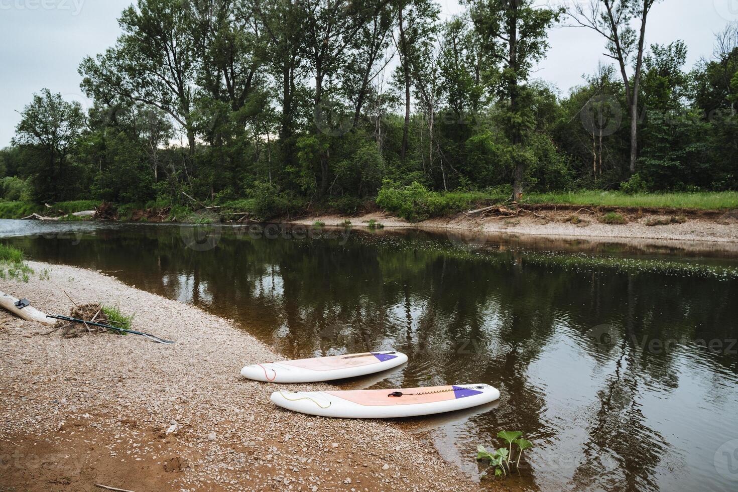 Two white SUP boards are parked on the river bank, sports camping equipment, supdording on a mountain river. photo