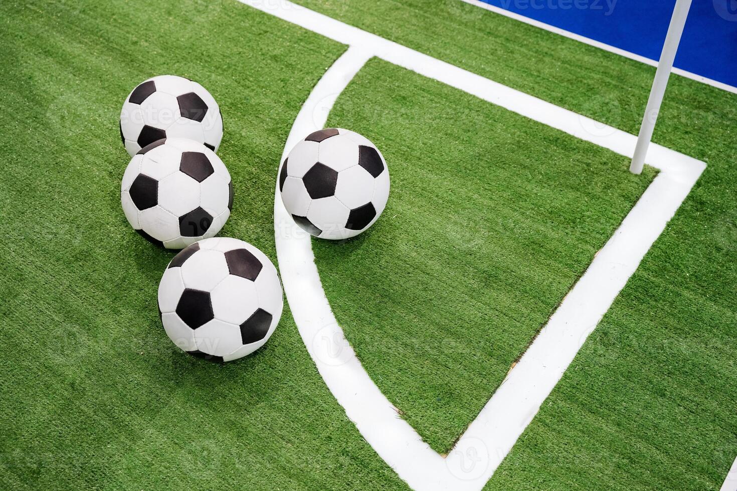 There are three soccer balls that are resting on the corner of a grassy soccer field, waiting to be used in an exciting game of soccer, also known as football in many countries photo