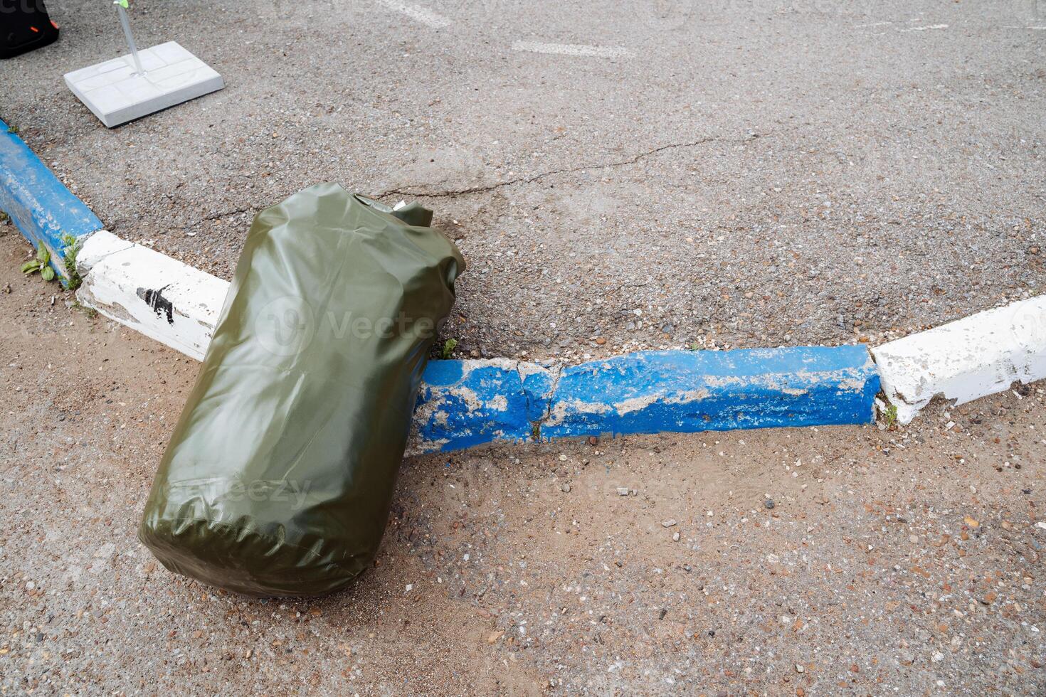 In the scene, a green bag is next to a blue and white line on the ground surrounded by asphalt, soil, wood, and hardwood flooring, creating a rich texture and color palette photo