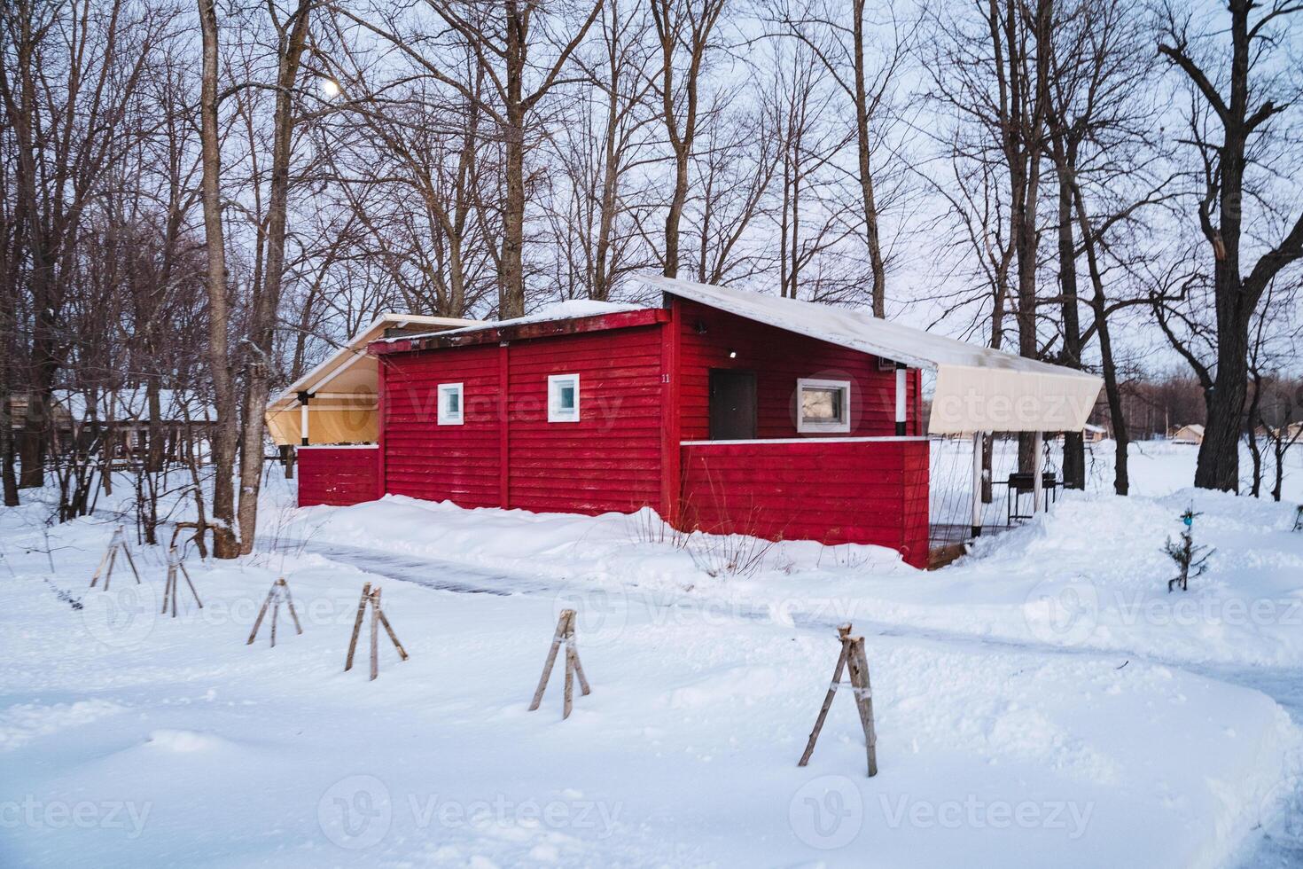 In this picturesque winter scene, a charming little red house is nestled cozily in the soft, fluffy white snow, with tall green trees nearby enhancing the natural beauty of the landscape photo