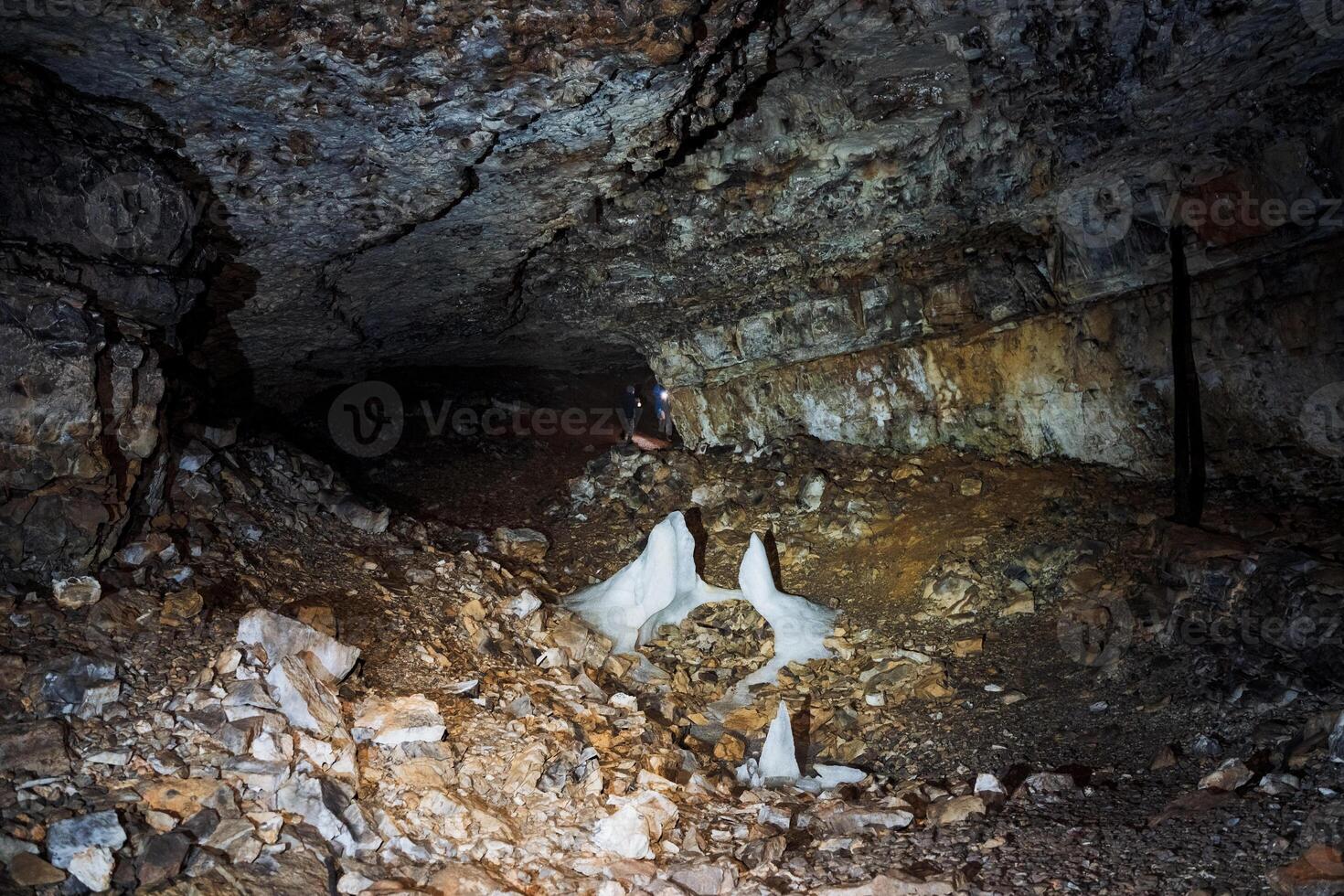 Inside a cave, there are numerous rocks scattered around, and there is also a source of light illuminating the ground, creating a unique atmosphere within the cavernous space photo