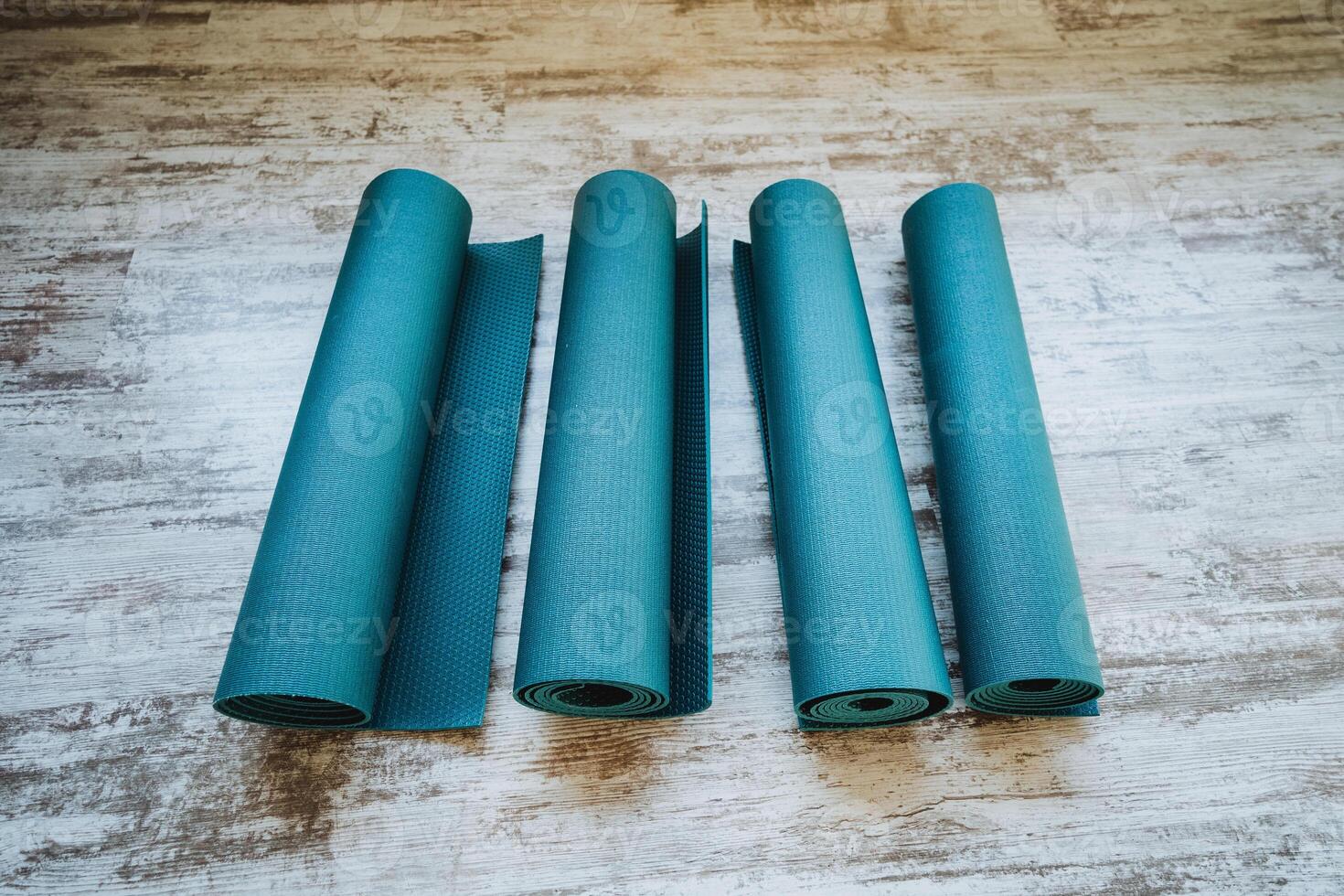 Four rolls of Azure yoga mats stacked on wooden floor photo