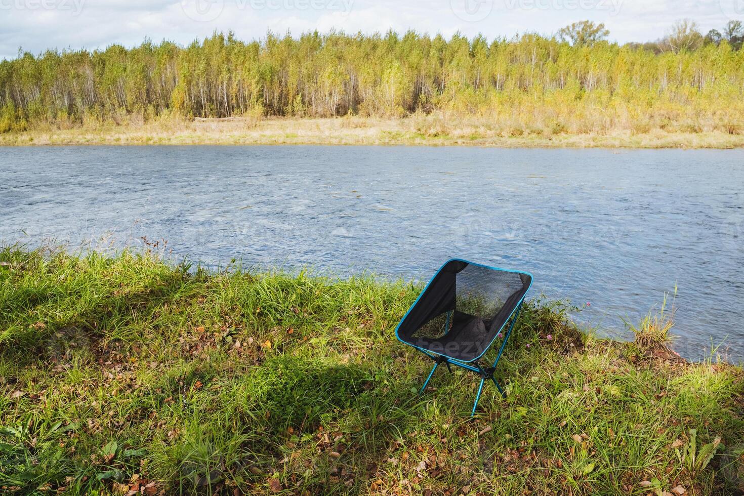 A rustic wooden chair on a grassy hill offers an exceptional view of a winding river below, capturing natures serene peace and inviting relaxation in this picturesque landscape photo