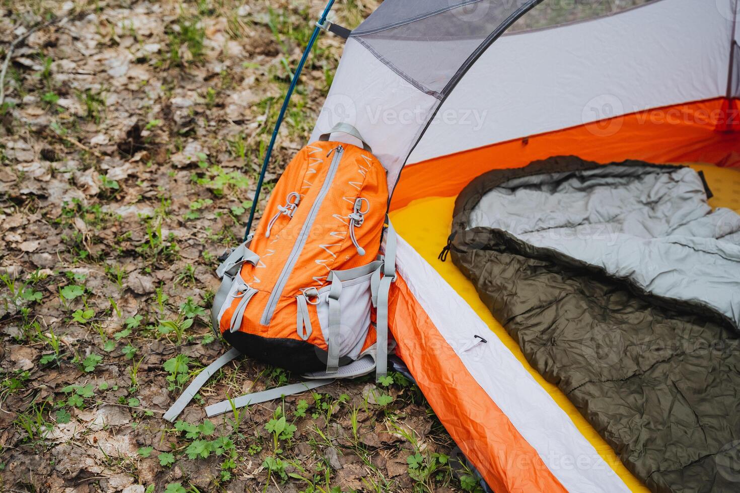 Tent with backpack and sleeping bag inside, next to motor vehicle on grass photo