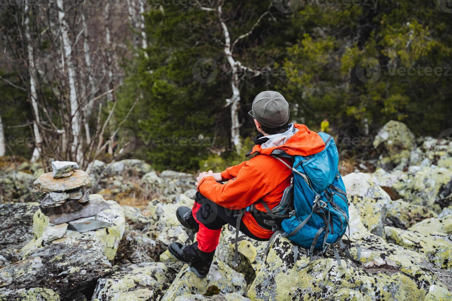 A man in a hat sits on bedrock in the forest, enjoying leisure time in nature photo