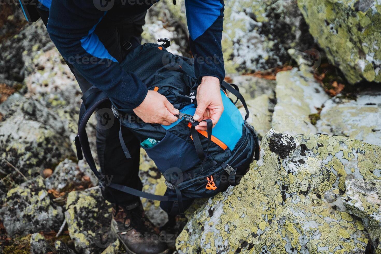 A person is putting something in a backpack on a rock photo