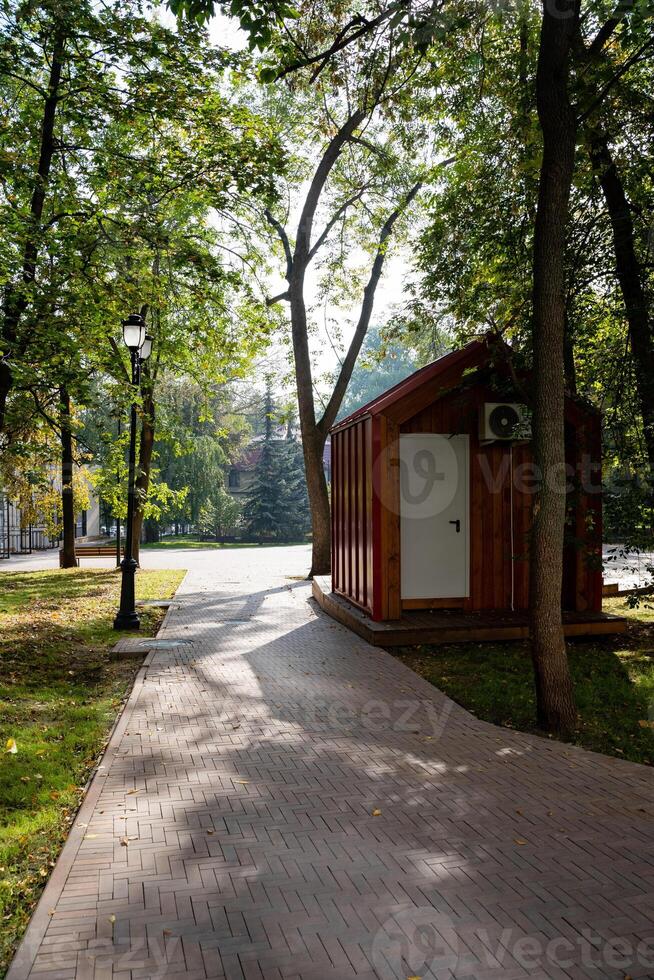 A charming and quaint small wooden shed is beautifully situated right beside a winding path that runs through a picturesque park, surrounded by lush greenery and scenic nature all around it photo