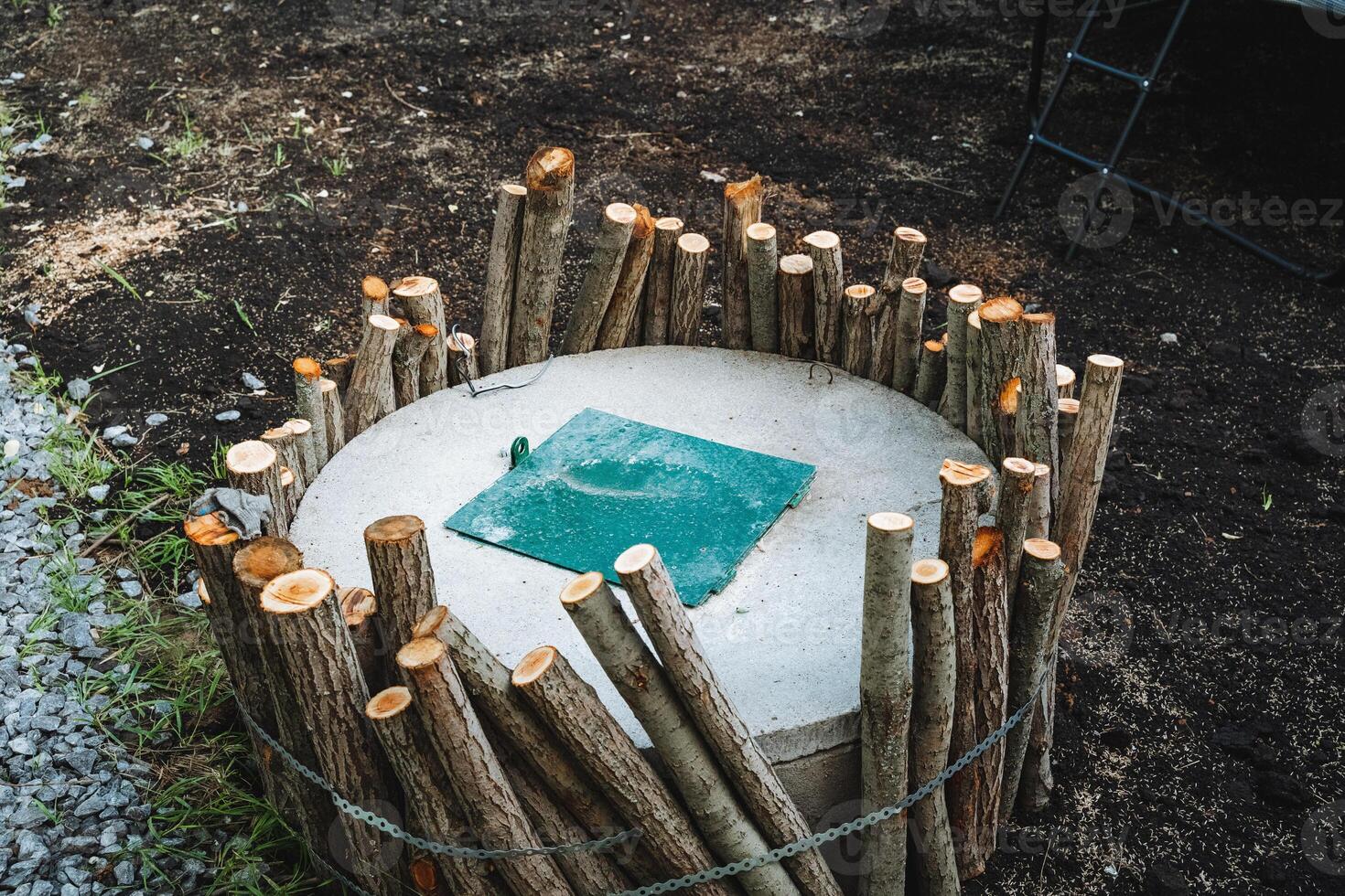 Nestled in a peaceful natural environment, a large concrete cylinder is surrounded by wooden poles and a vibrant green tarp, forming a unique and creatively designed structure photo