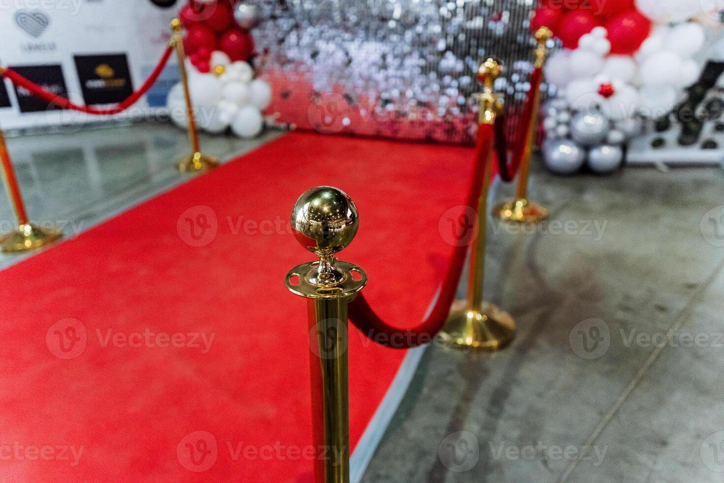The red carpet is lined with gold poles and balloons for the event photo