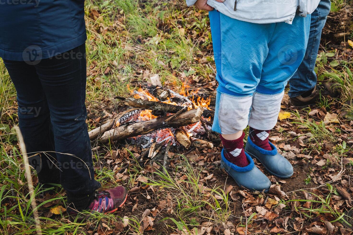 A person is standing closely beside a child in front of a blazing fire, which adds a cozy warmth and illumination to the memorable moment they are experiencing together outdoors photo