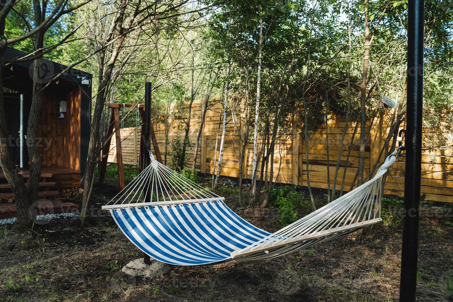 A hammock with calming blue and white stripes gently sways in a peaceful forest, offering a serene spot to relax in natures beauty and find tranquility amid a lush green environment photo